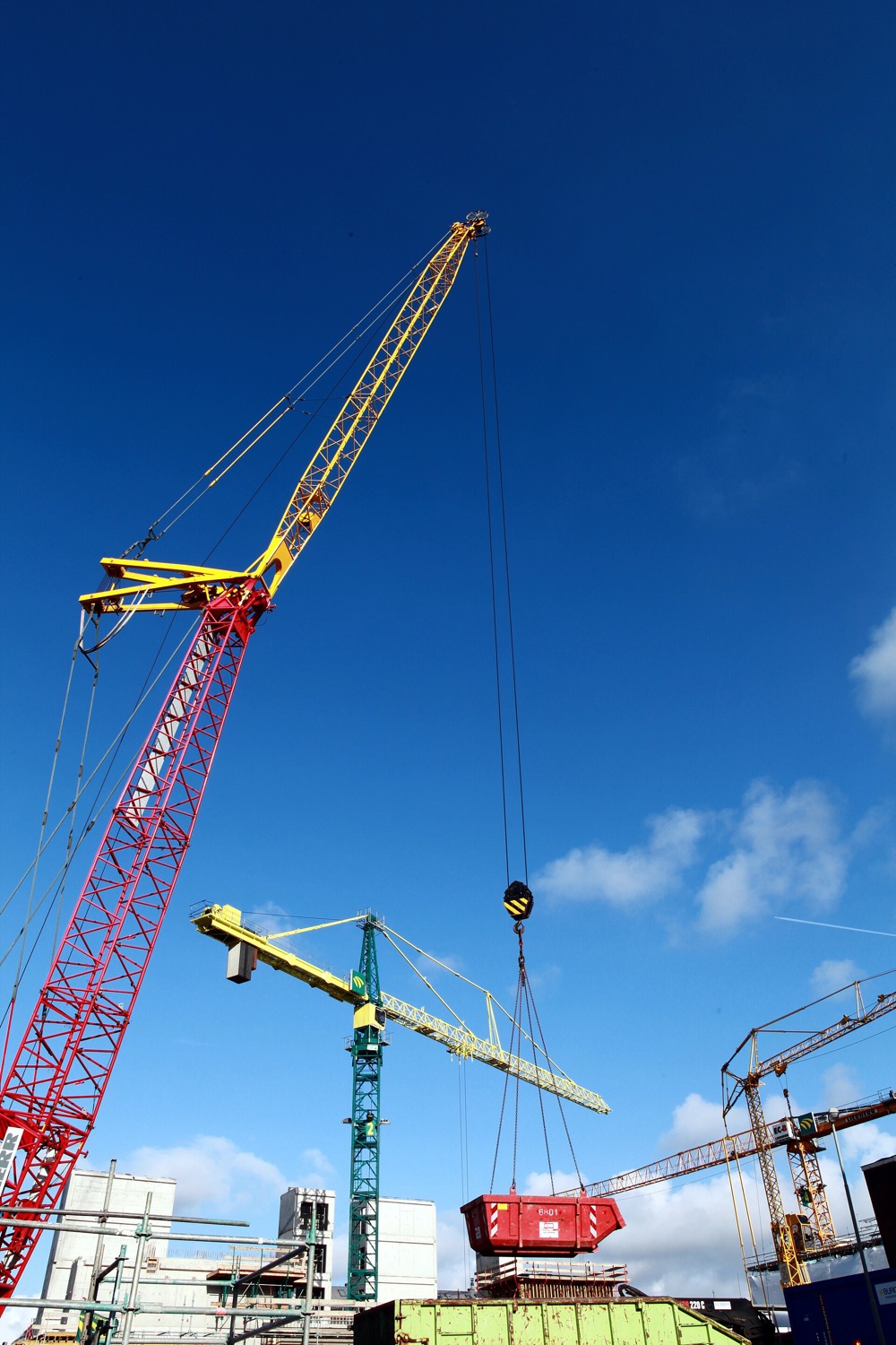 Grúas torre trabajando sobre una obra en construcción, contra un cielo azul.